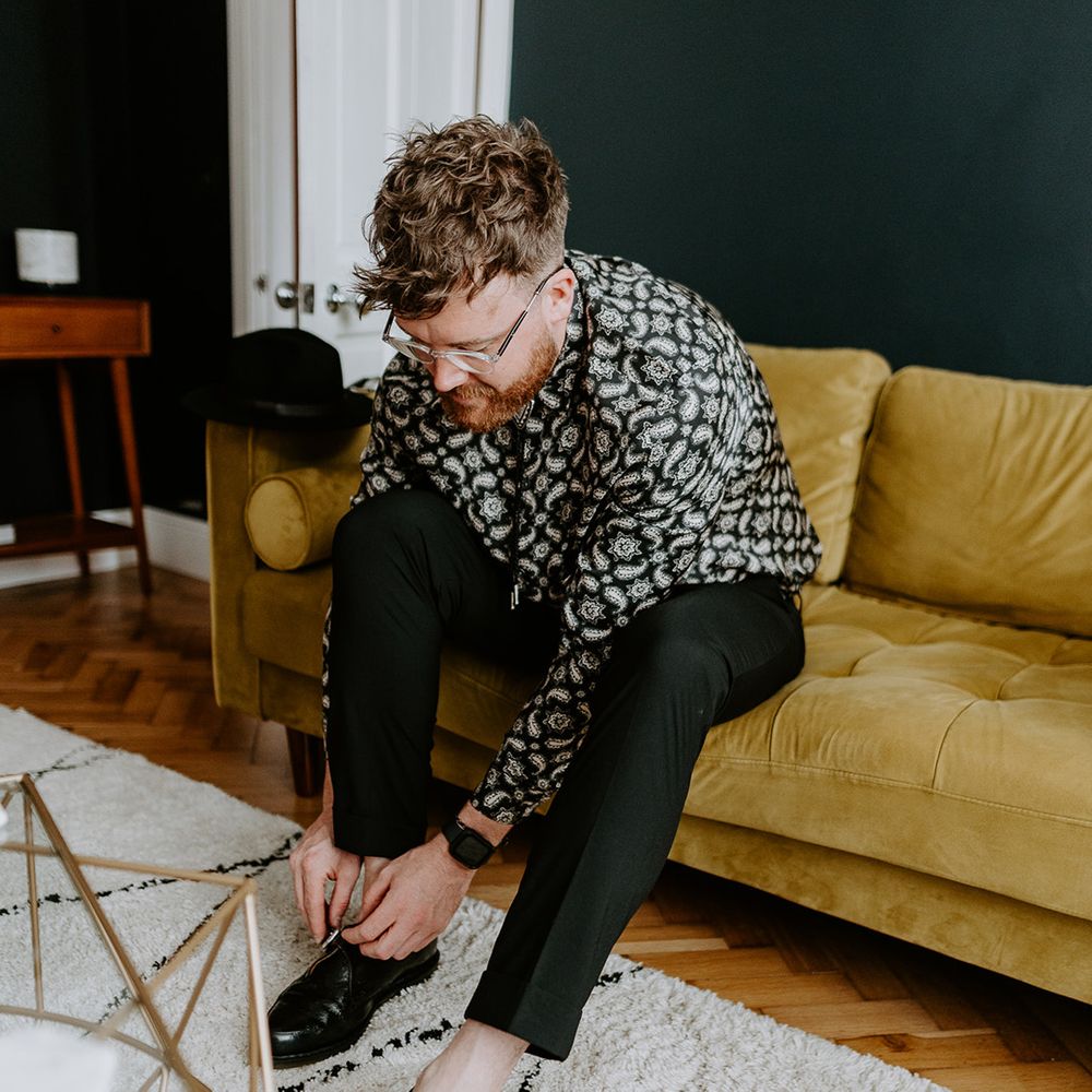 Groom gets ready on the morning of his wedding day whilst wearing patterned shirts and black trousers 