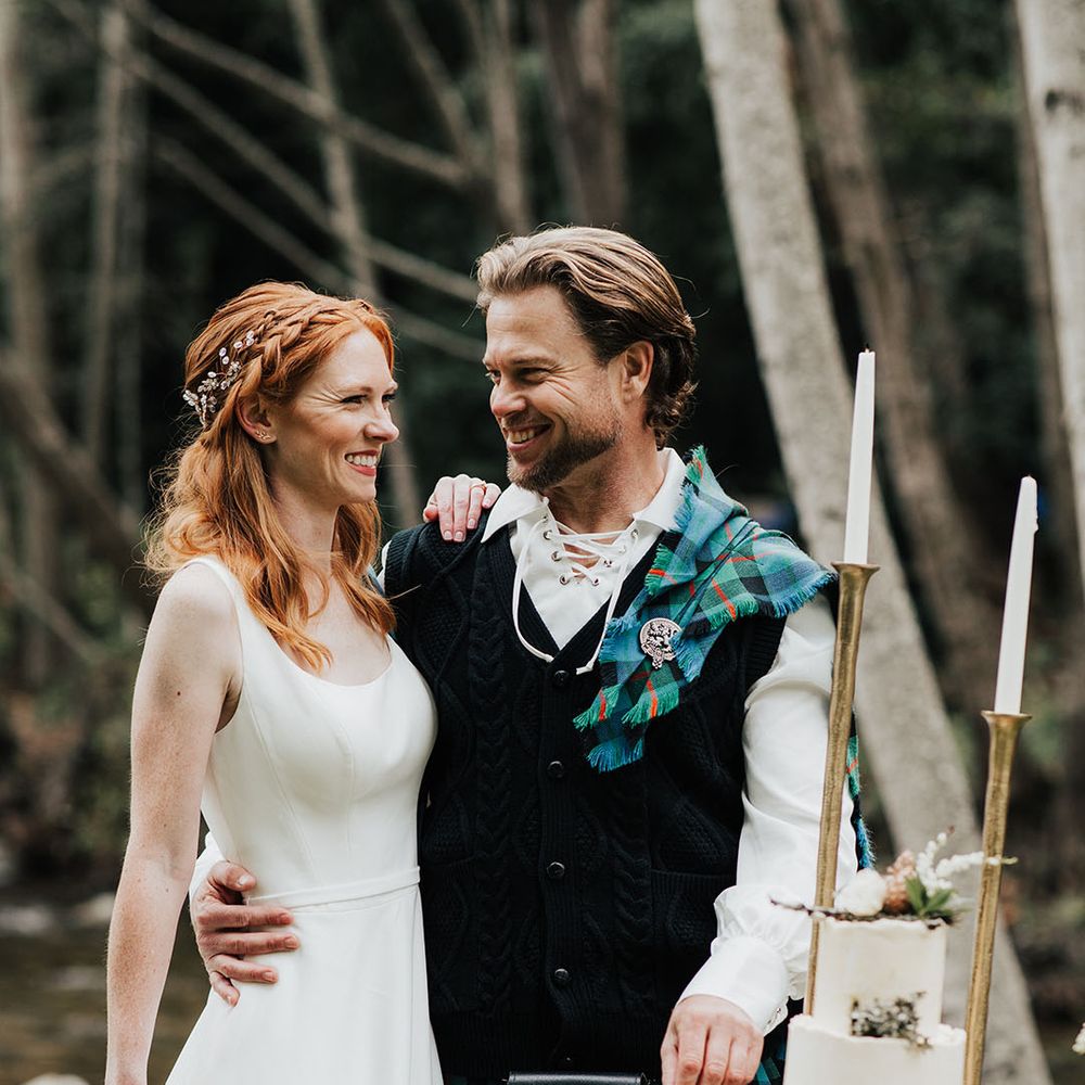 Groom in a kilt, sporran and aran embracing his bride with red hair in a princess wedding dress 