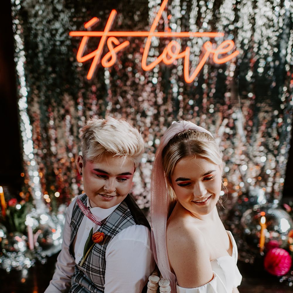 Two brides sitting back to back on chairs wearing a grey check suit and jumpsuit at Highfield House