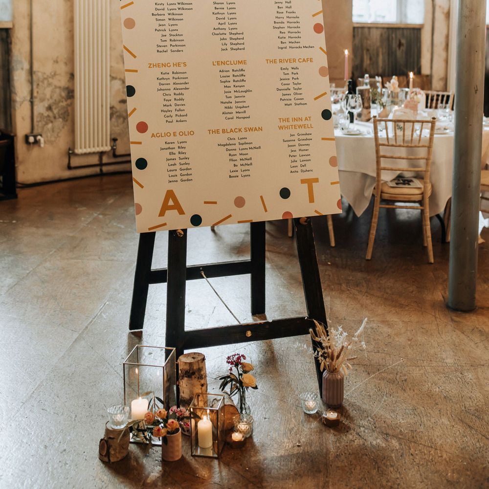 Modern wedding table plan with bold confetti pattern on black easel fo industrial style wedding reception at Holmes Mill wedding venue