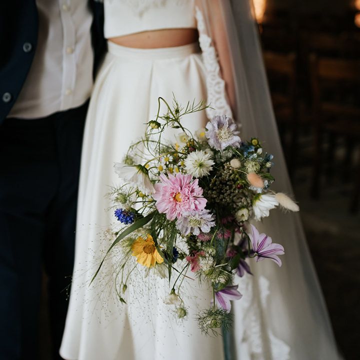Bride holding colourful wedding bouquet of assorted flowers wearing pleated high low skirt
