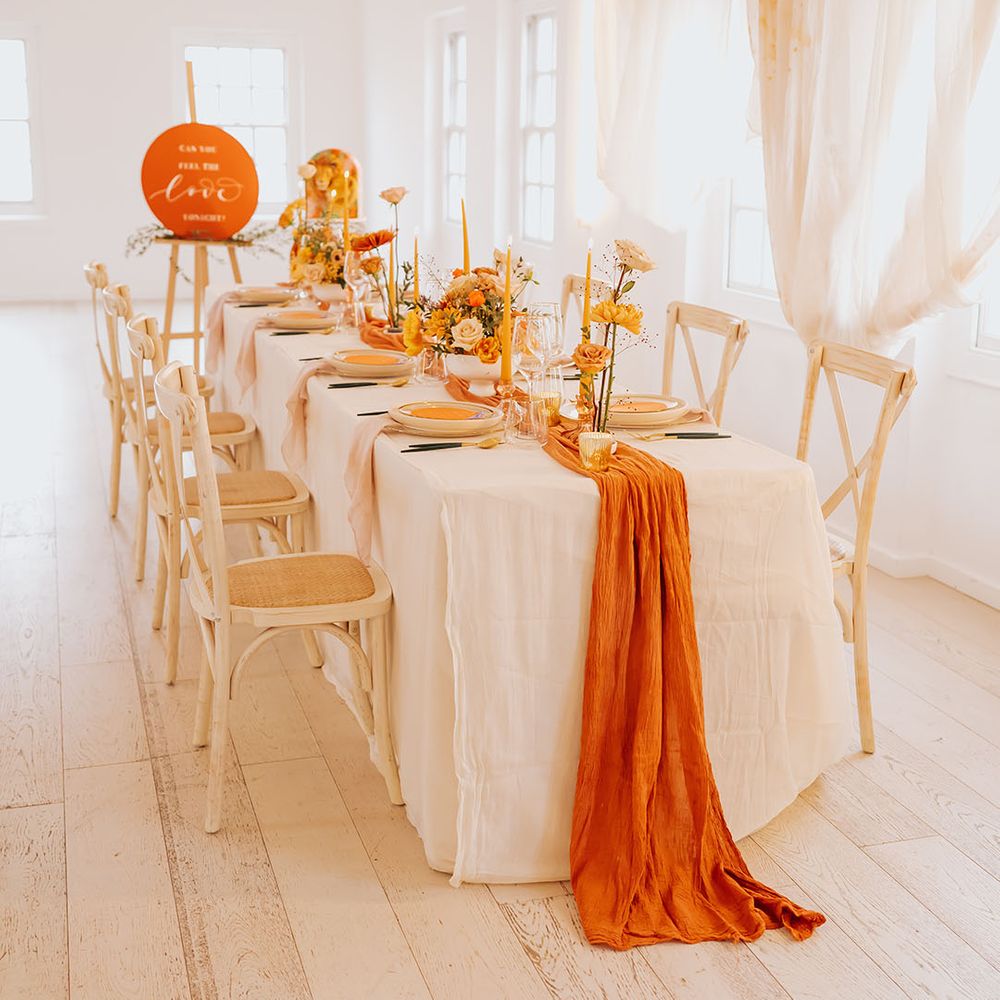 golden wedding table decor with an orange table runner, yellow taper candles and flower arrangements and gold cutlery 