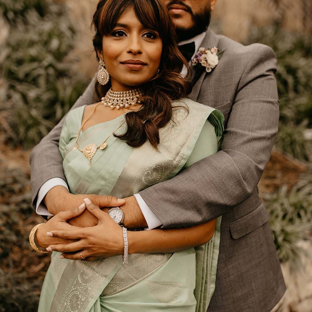 Groom in grey suit with arms wrapped around new bride in mint green saree 