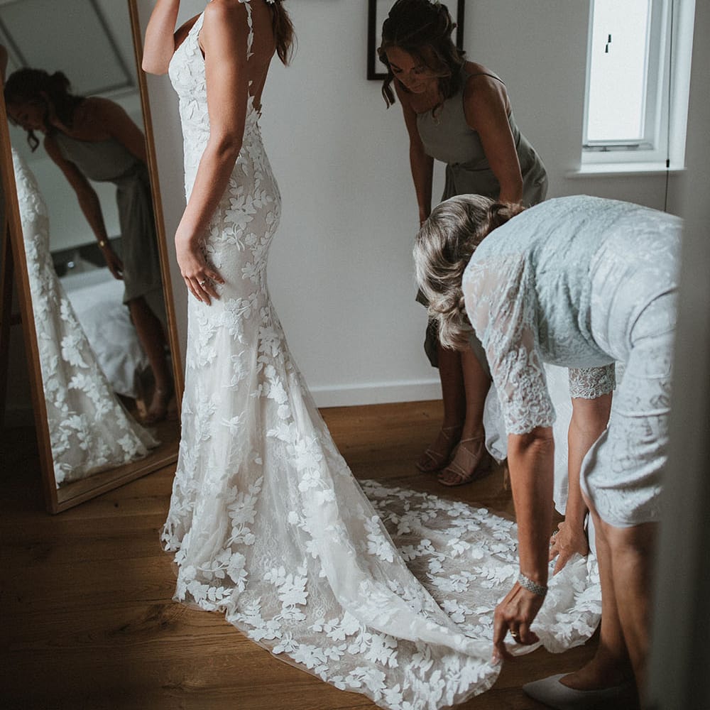 Bride wears her red hair tied back with fishtail braids to either side and embellished hair accessories are pinned to the back 