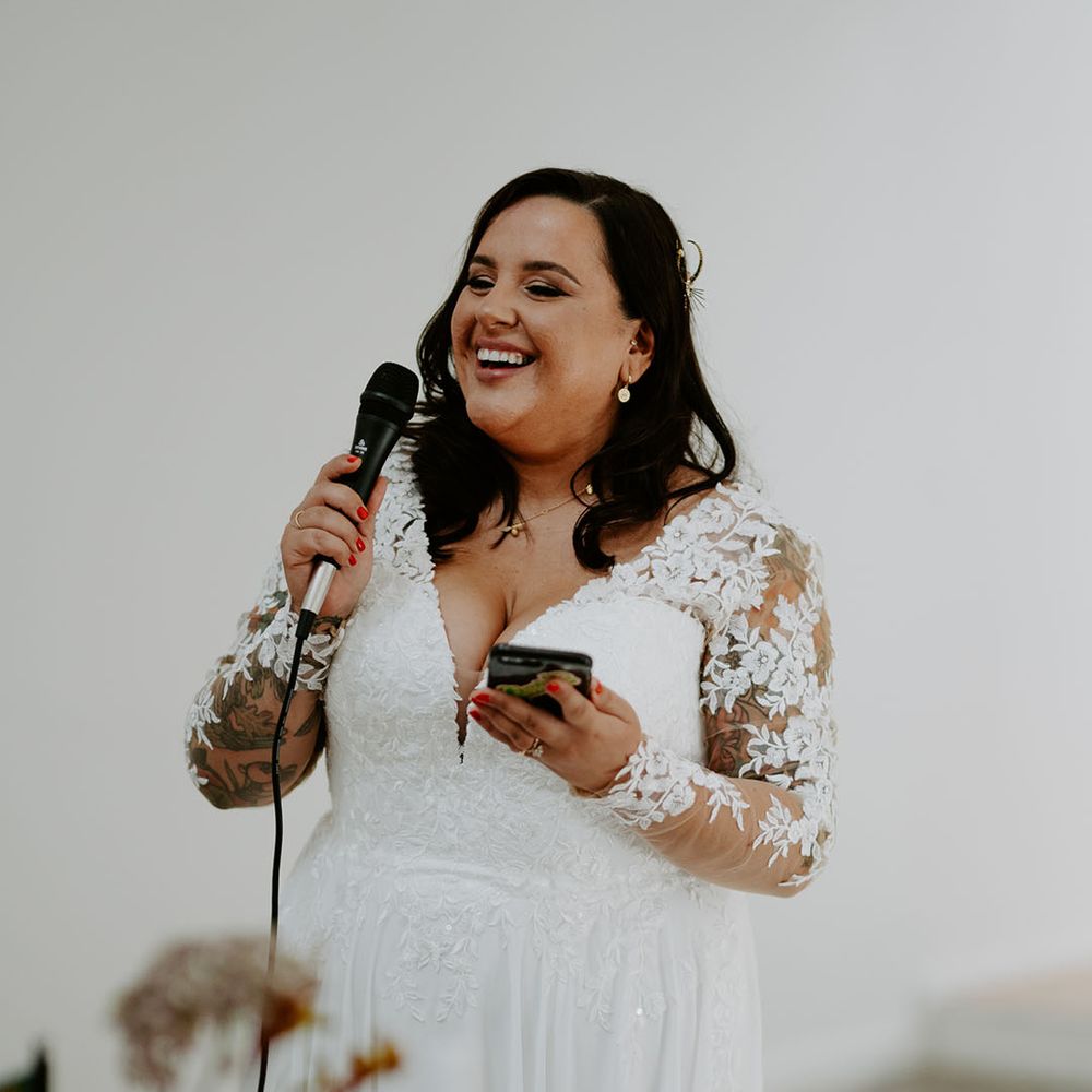 Bride wears long sleeve lace wedding dress and gives speech during reception 