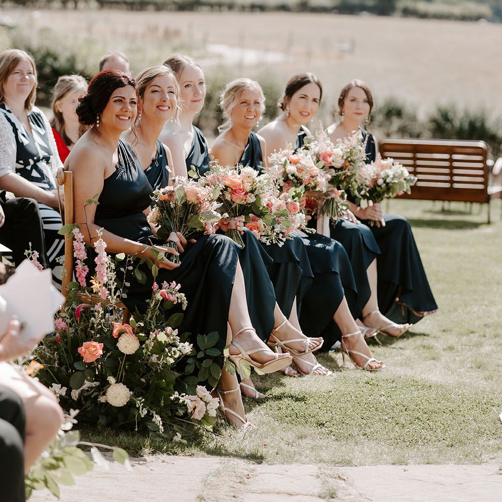 Bridesmaids wear cold shoulder dresses as they hold brightly coloured floral bouquets 