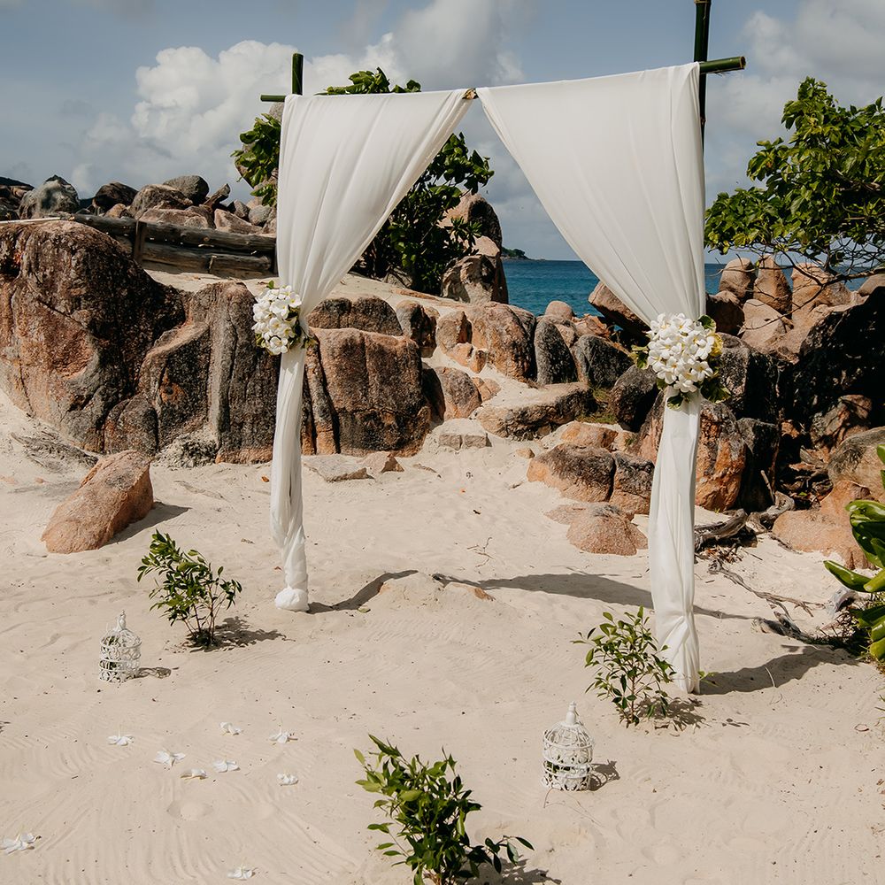 Fabric chiffon white wedding arch with tropical flower decorations attached and bunches of tropical syzygium formosanum 
