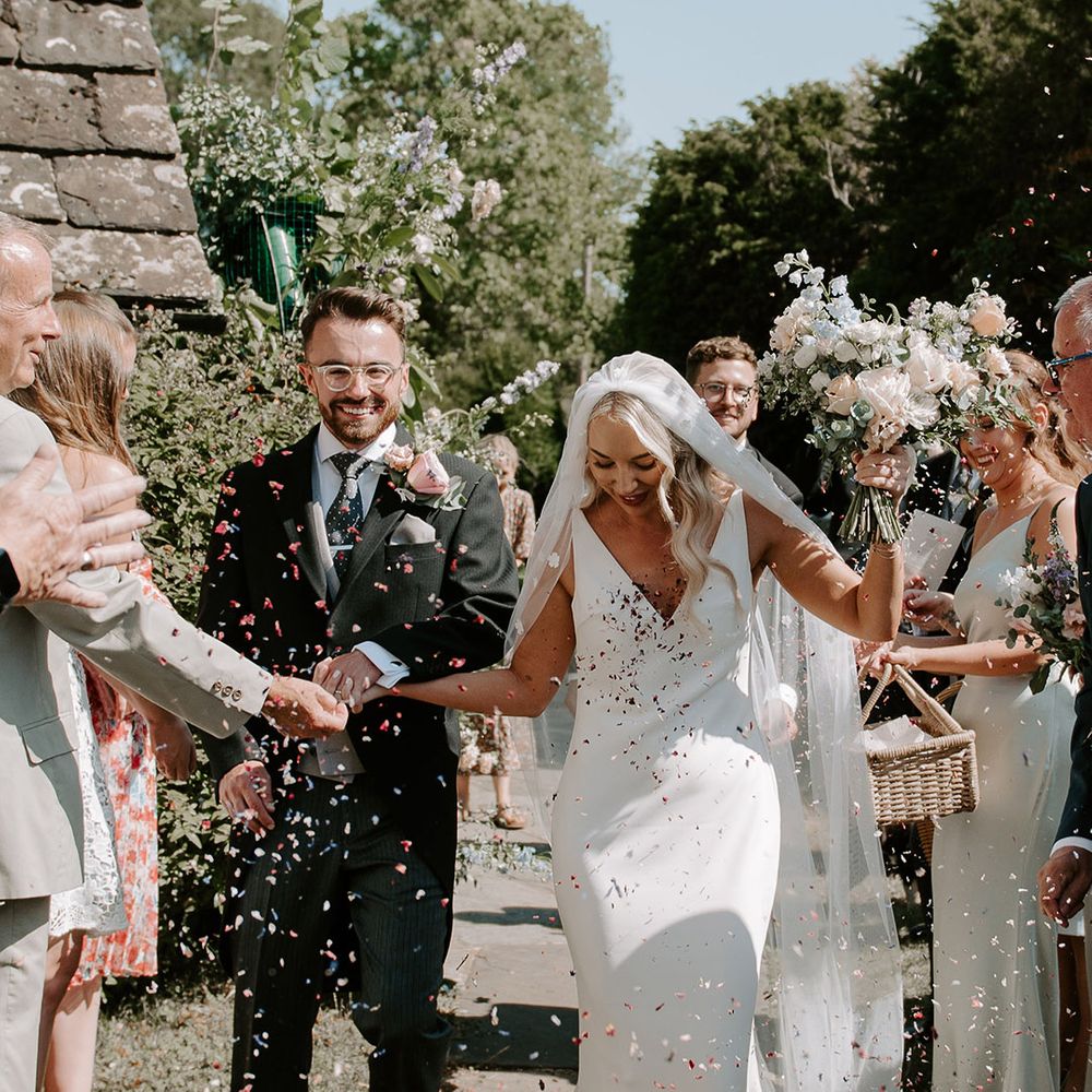 Groom in three piece suit with a large pink buttonhole with the bride in a Made With Love wedding dress have confetti moment 