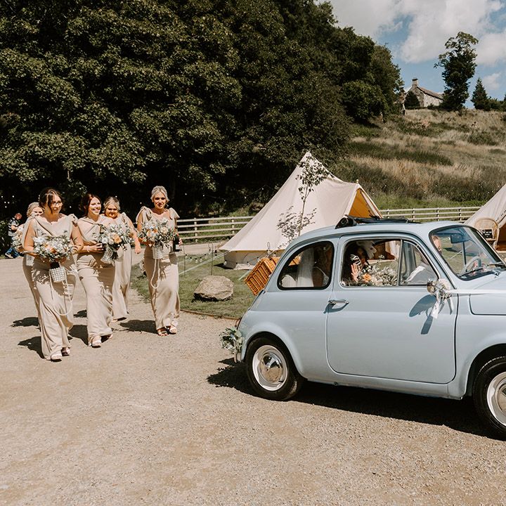 The bride makes her way to the ceremony in a baby blue vintage Fiat 500 wedding car followed by the bridesmaids in gold bridesmaid dresses