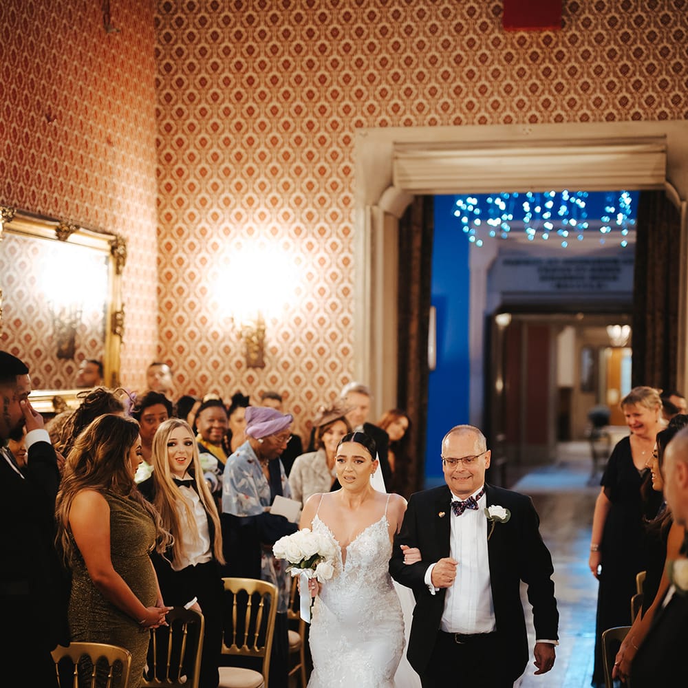 Father of the bride walking bride in sleeveless v neck Enzoani wedding dress with tulle finish and church length veil down the aisle of Grittleton House wedding venue 