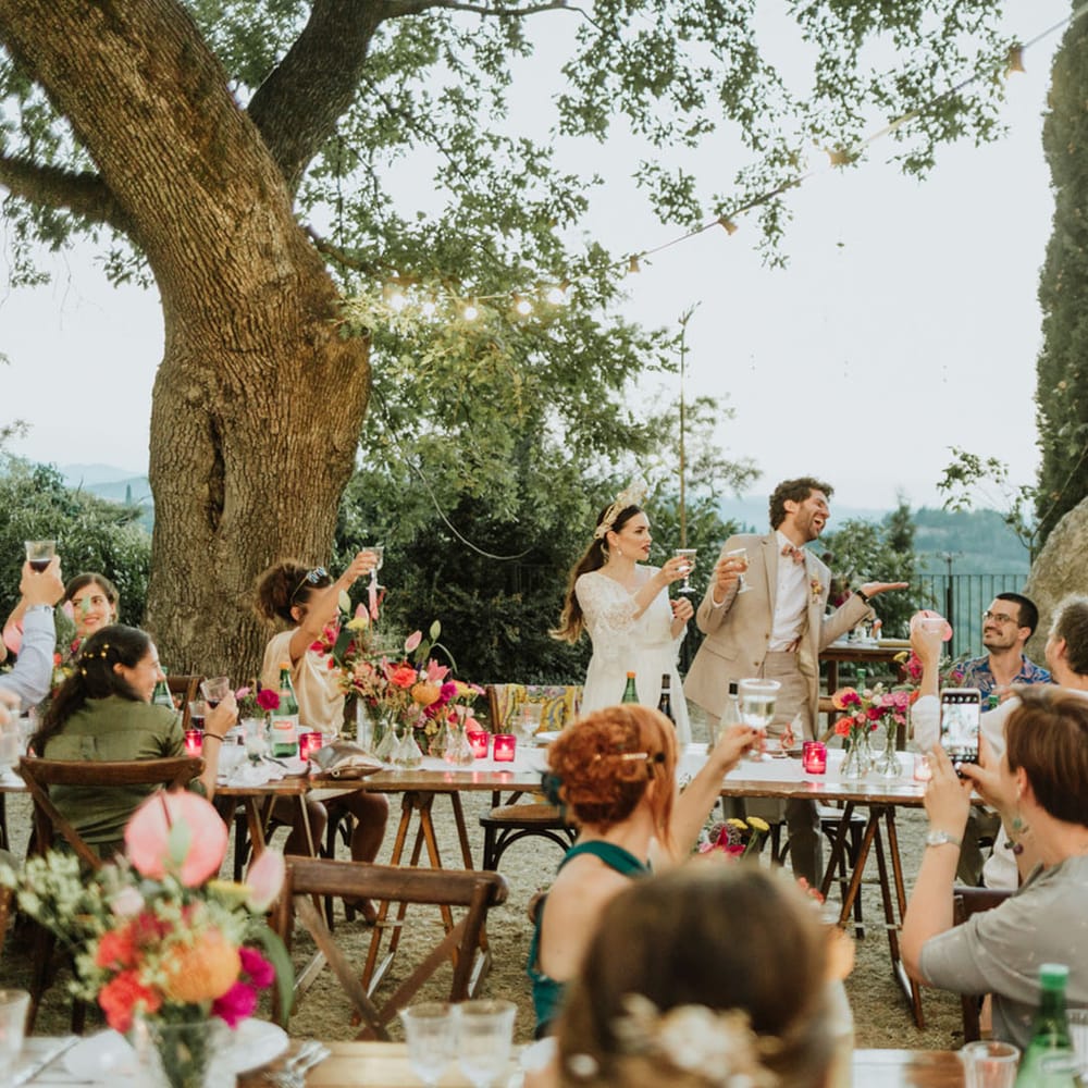 Bride and groom cheersing wedding guests at destination wedding breakfast in Italian hills.
