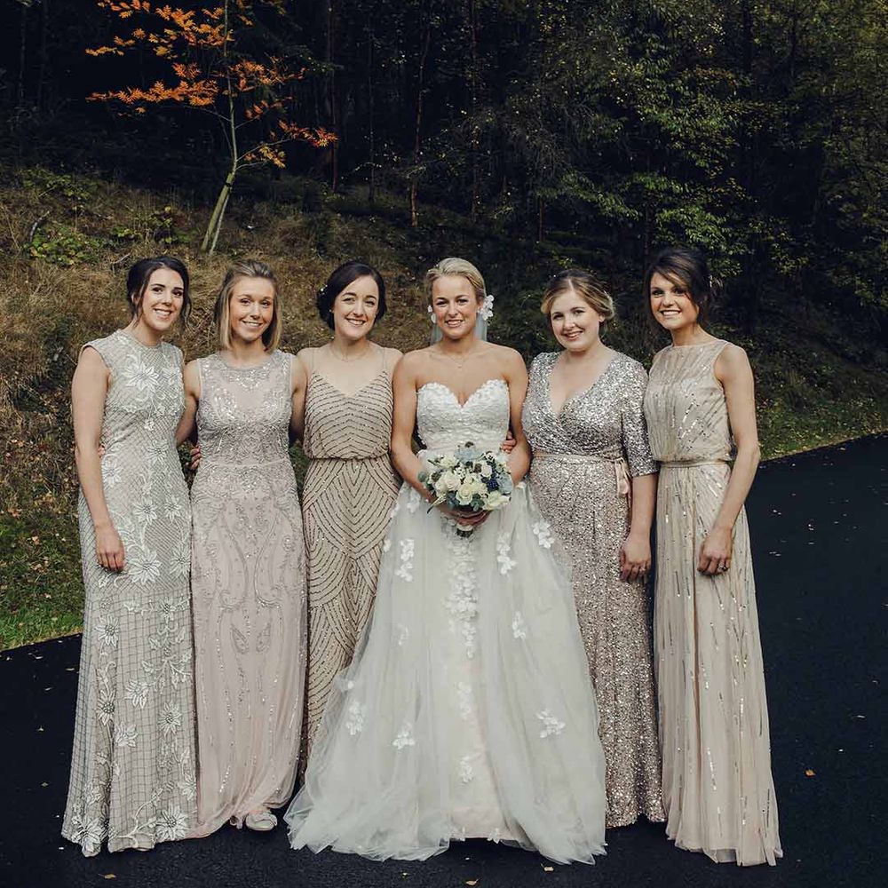 Bride in sweetheart neckline strapless wedding dress standing with bridal party in mismatched embellished bridesmaid dresses