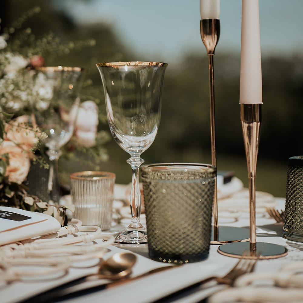 Gold rimmed glassware, gold candleholders with white taper candles and pink and white flower arrangements 