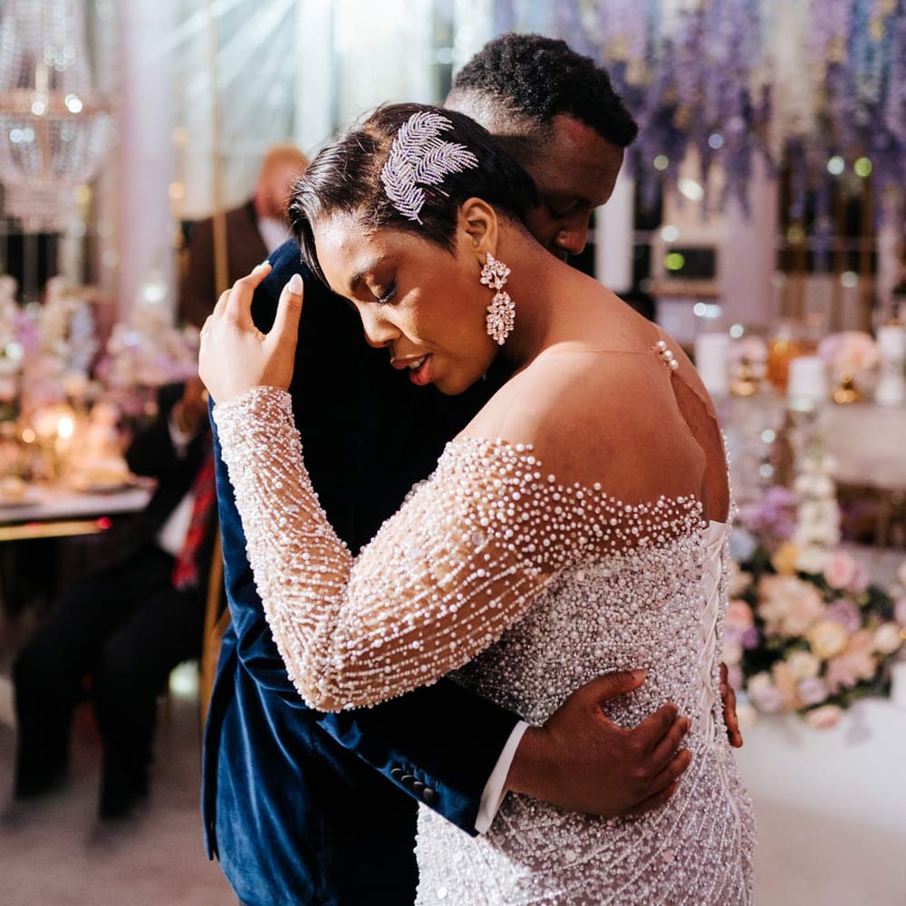 Groom in midnight velvet grooms suit dancing with bride in illusion v neck sheer off shoulder long sleeve pearl embellished wedding gown and large silver bridal hair accessory
