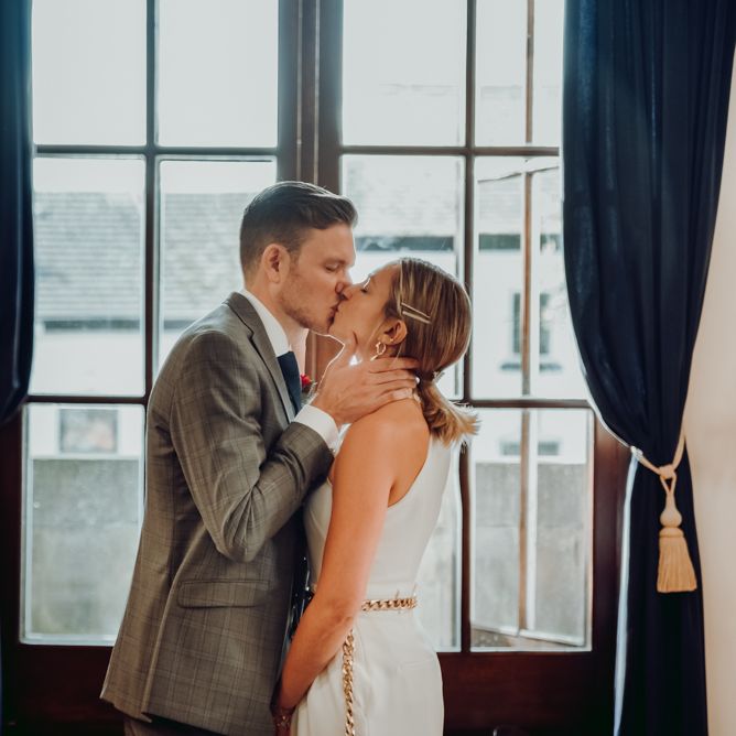 Groom kissing his bride in a Massimo Dutti jumpsuit for intimate micro wedding ceremony 
