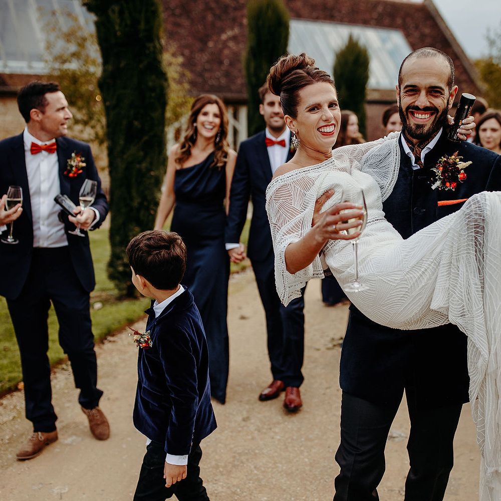 Groom carries bride through gardens after wedding ceremony