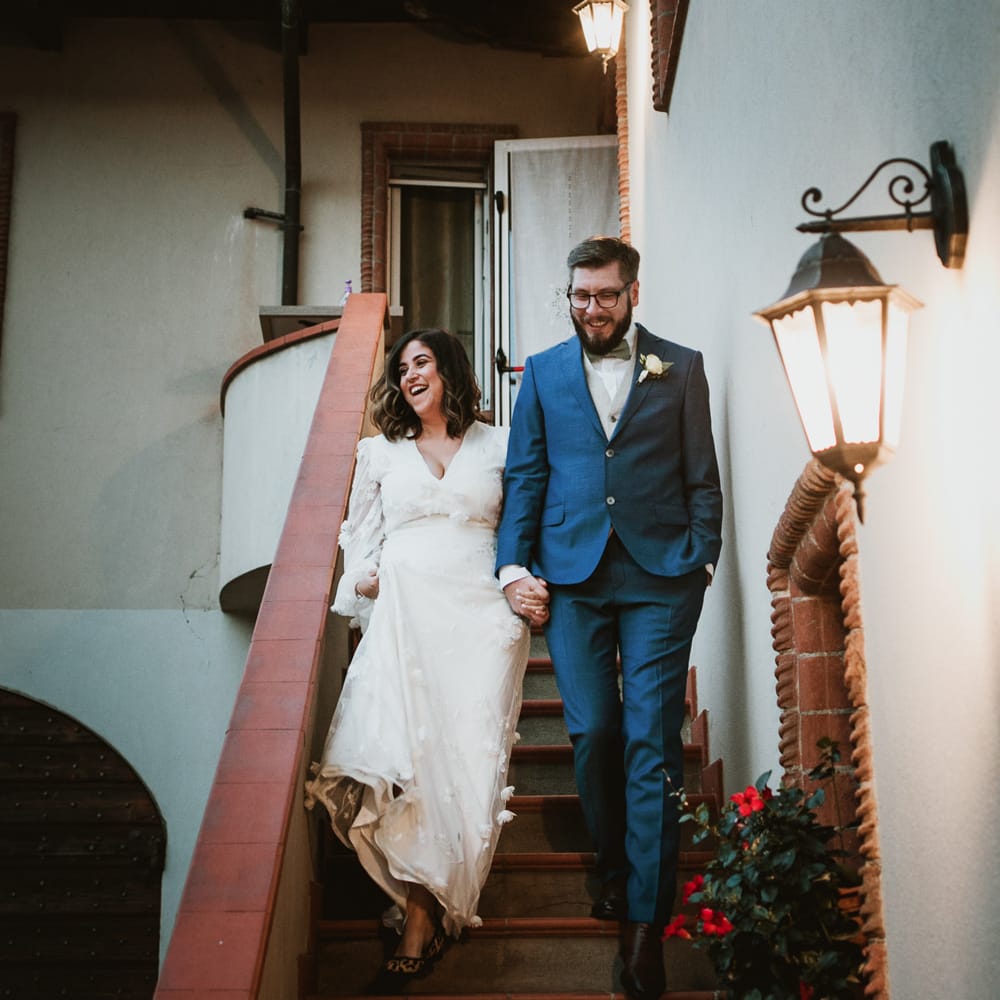 Bride in a white wedding dress with flowers detail walking down the steps holding hands with her groom in a navy blue suit