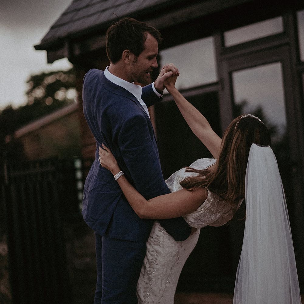 Groom dips bride as they dance outdoors during their wedding reception