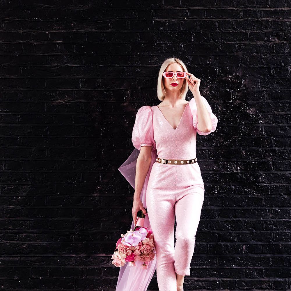 Bride in a fitted pink jumpsuit with gold belt and blush bouquet 