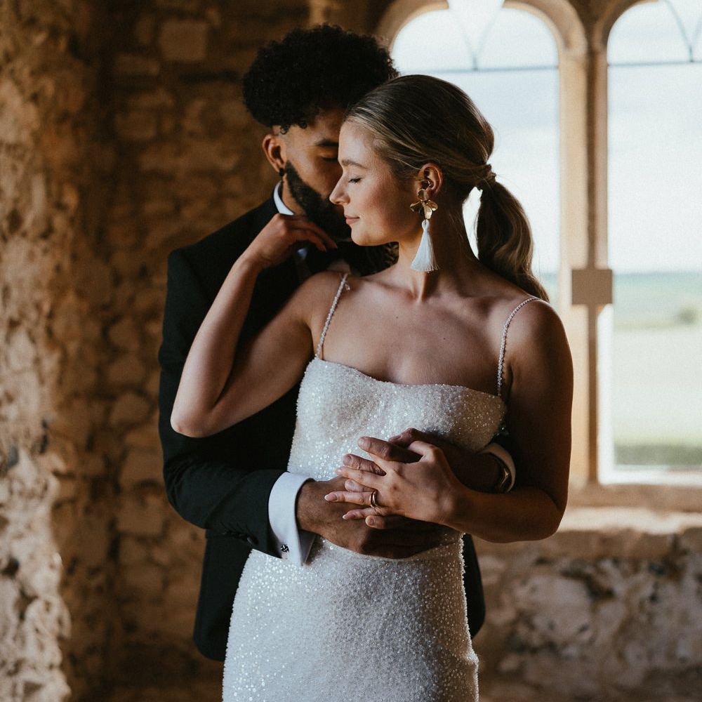 Groom in a black tuxedo embracing his bride in a sparkly wedding dress and tassel earrings 