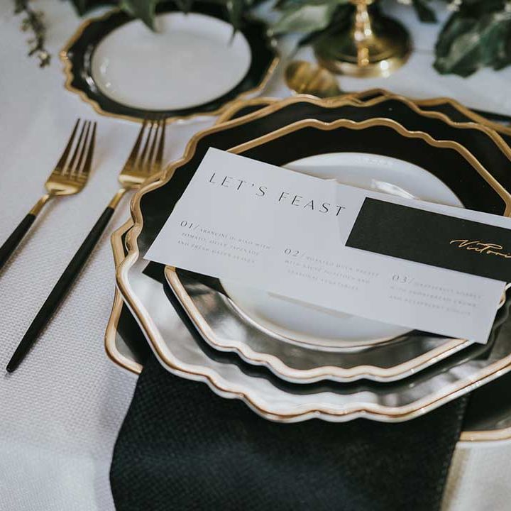 Sophisticated place setting with black and white plates with gold rim and black and gold cutlery 