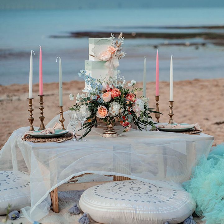 Bride in a mint green tulle wedding dress sitting at her relaxed beach wedding reception decorated with pastel flowers, decor and cakes 