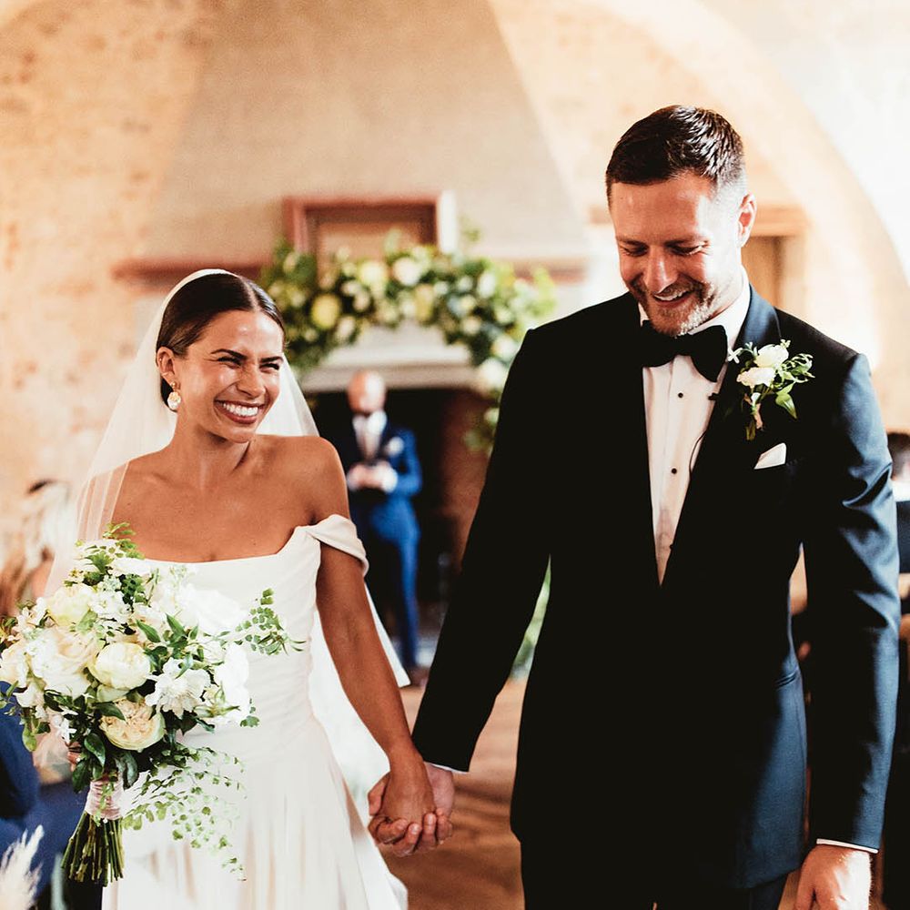 Bride & groom walk hand in hand down the aisle as bride wears Halfpenny London veil