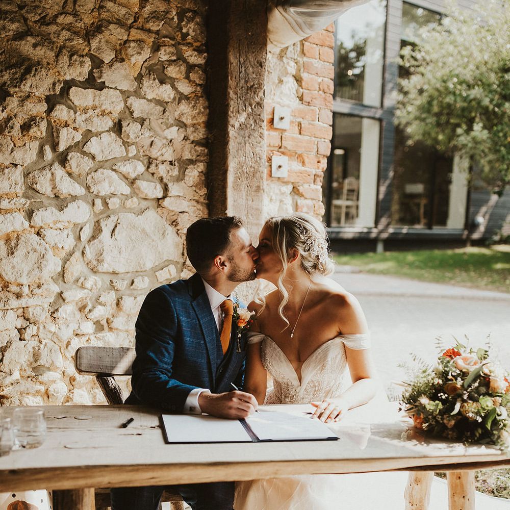 Bride and groom kiss as they sign a register