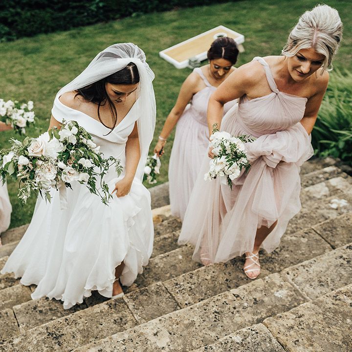 Bridal party in dusky pink TH&TH bridesmaid dresses walking up the steps of Foxhill Manor with the bride in a Suzanne Neville wedding dress