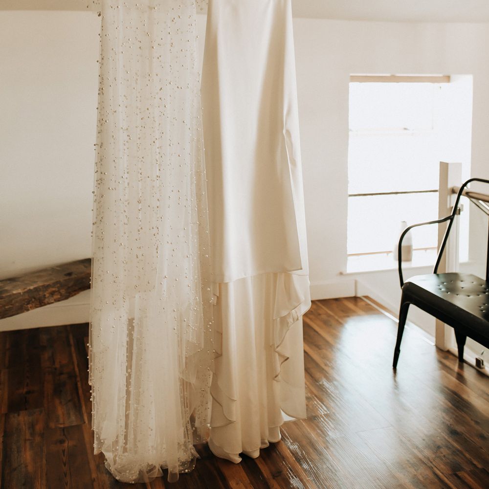 White cami wedding dress with mesh overlay encrusted with pearls hanging from beam