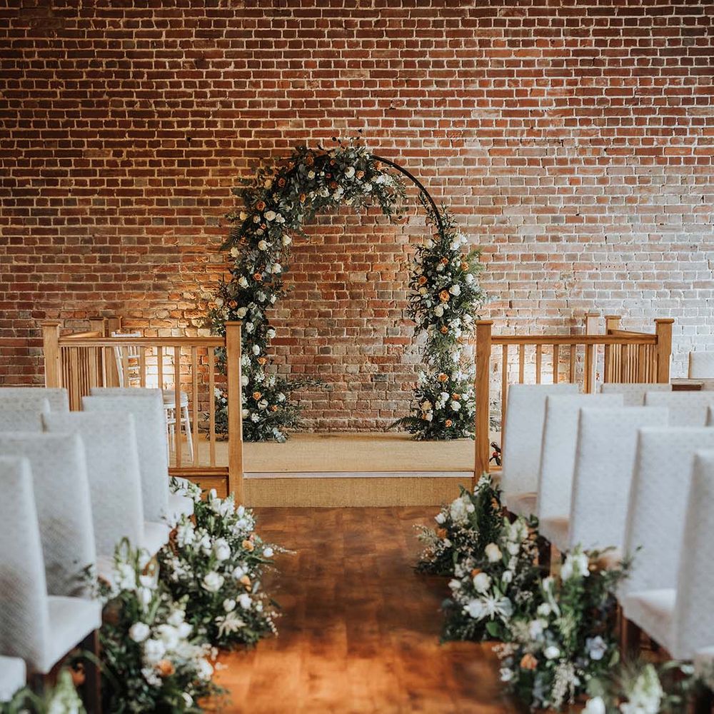 Aisle and altar style with white high back chairs and white and orange flowers with flower archway