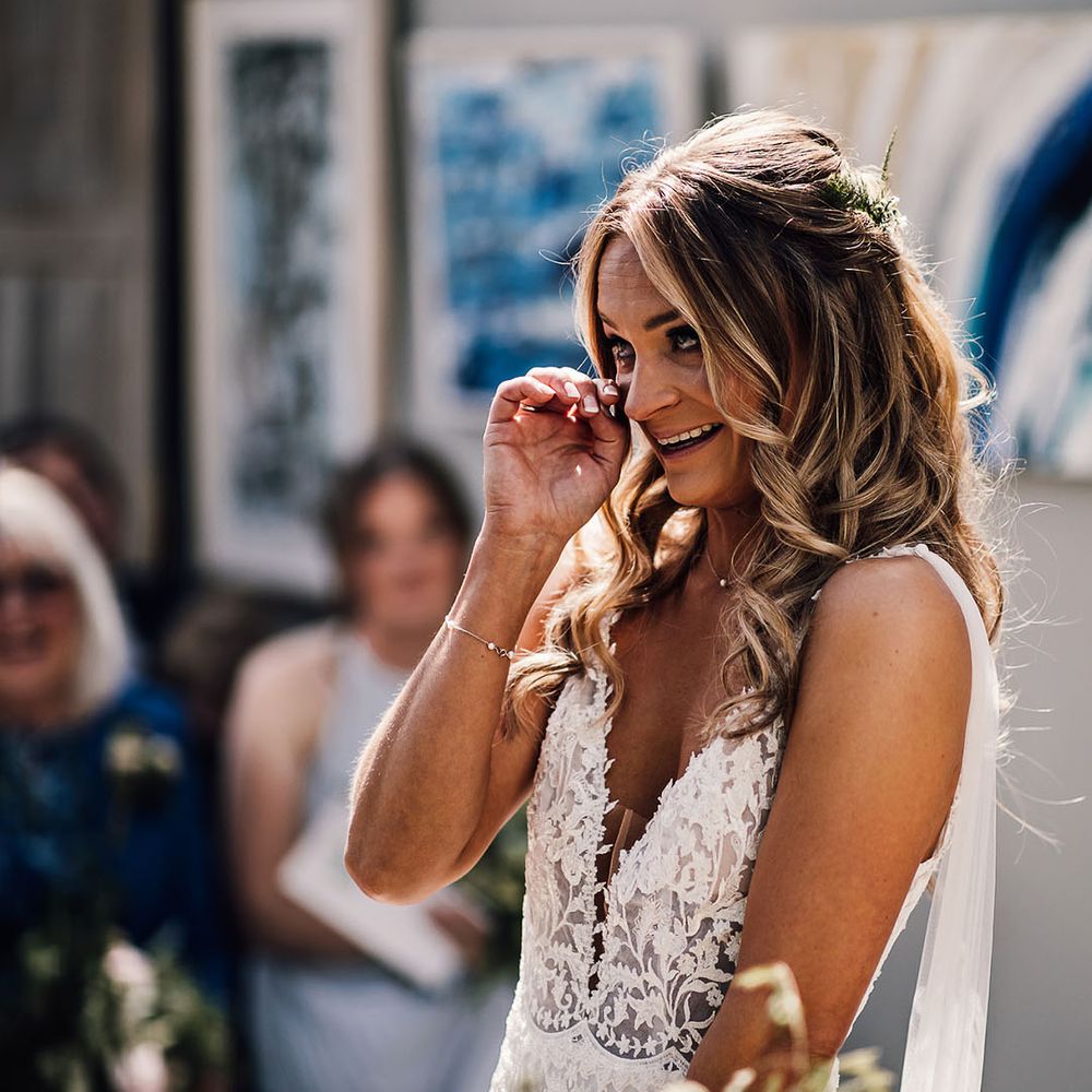 Bride in lace v neck wedding dress with tulle wings wipes her eyes during ceremony 