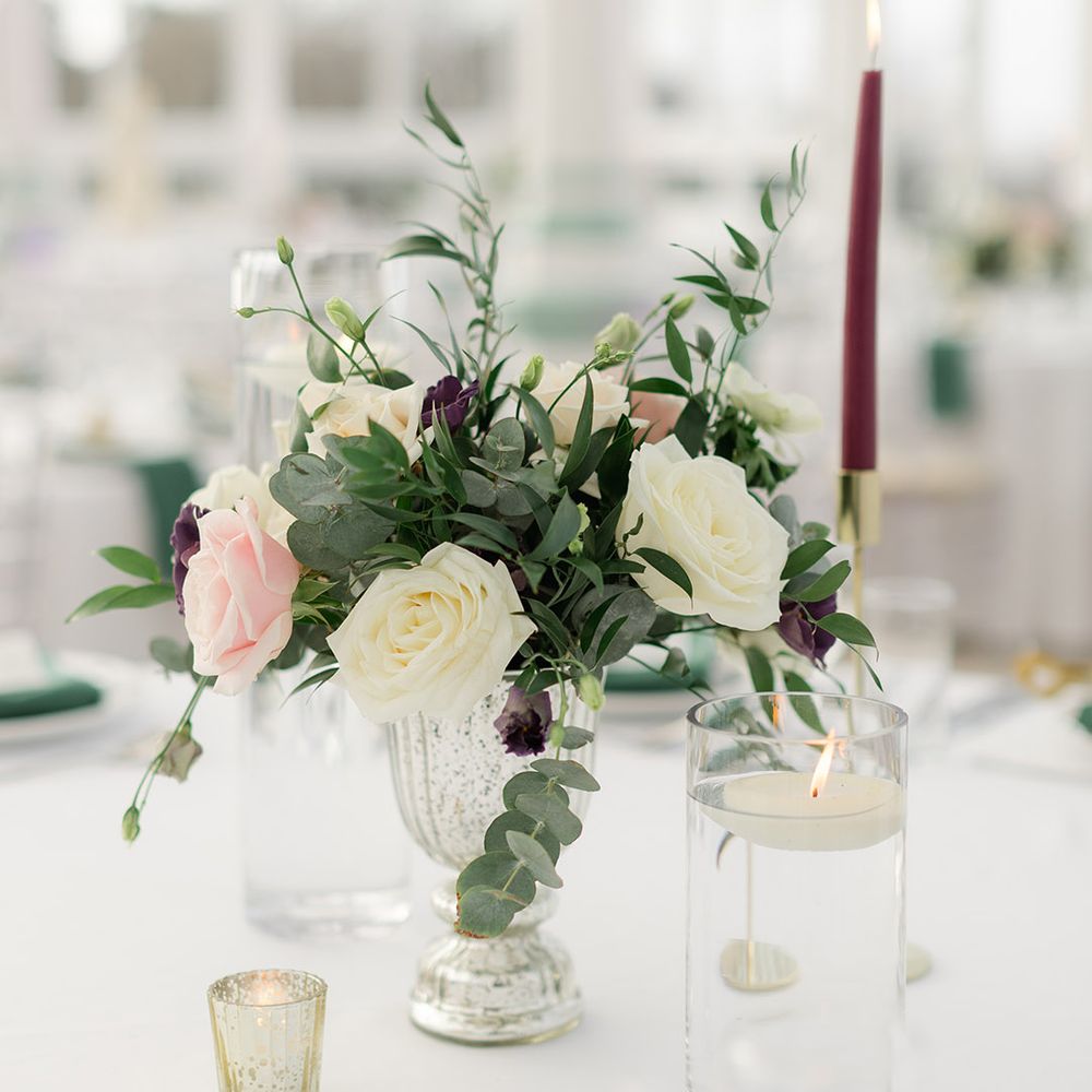 White & pale pink roses sit in vase beside candles placed on white tablecloths 