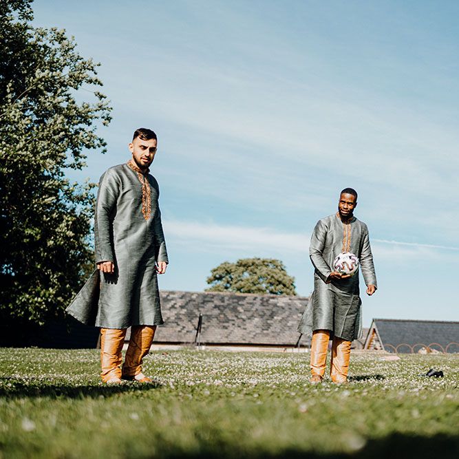 Groomsmen wear traditional sherwanis whilst playing a game of football outdoors 