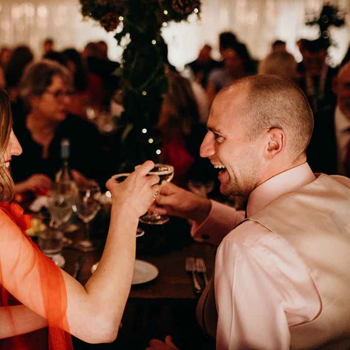 Bride with 3d appliqué red wedding cape and groom saying cheers with their wedding cocktails