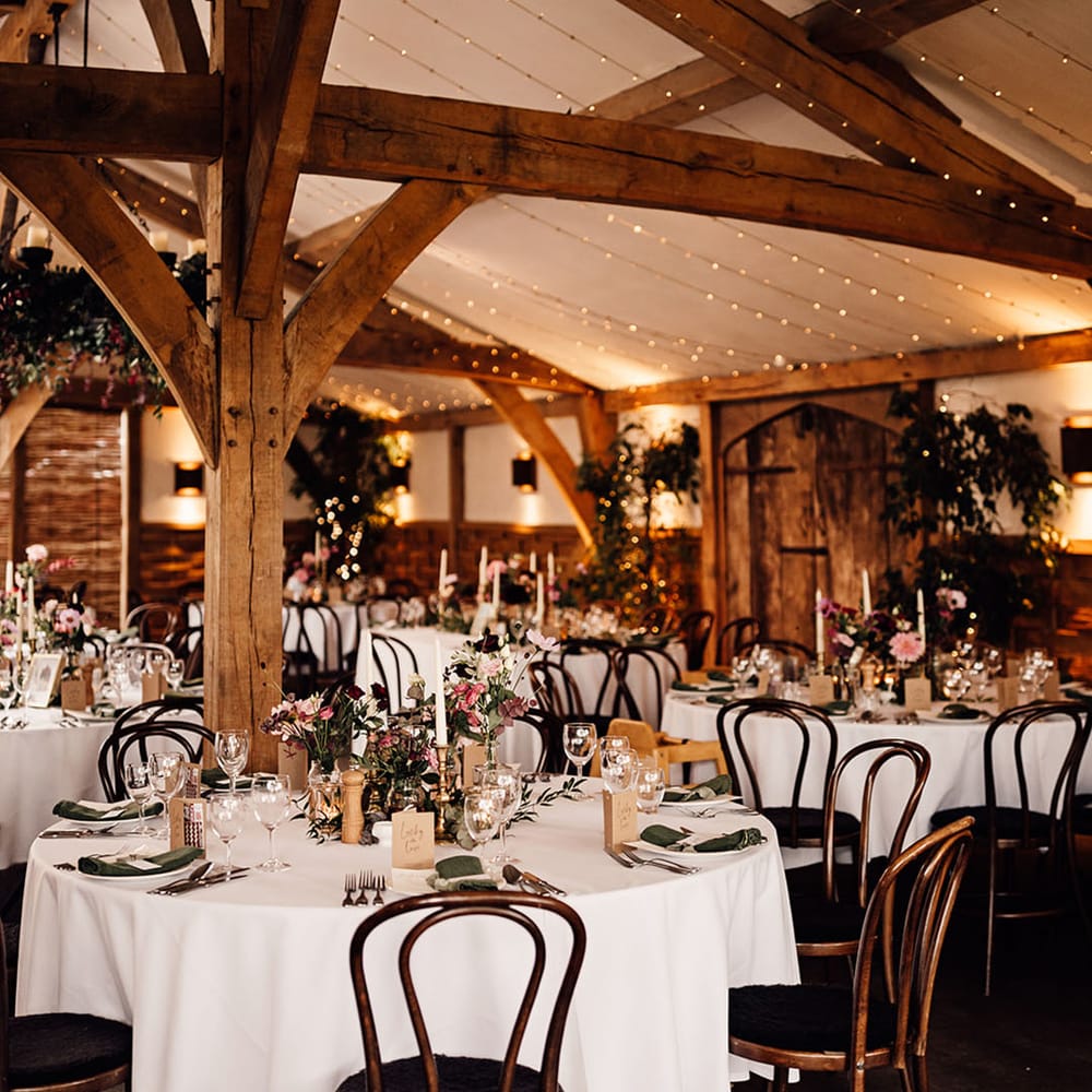 Cripps Barn wedding venue with fairy lights decorating the top of the venue and plenty of pink and purple flowers 