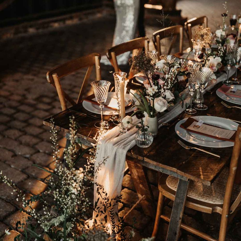 Bride and groom dancing by ustic luxe wedding tablescape with white fabric table runner, large foliage, baby's breath, garden rose and eucalyptus floral arrangements, tapered candles and ceramic vases 