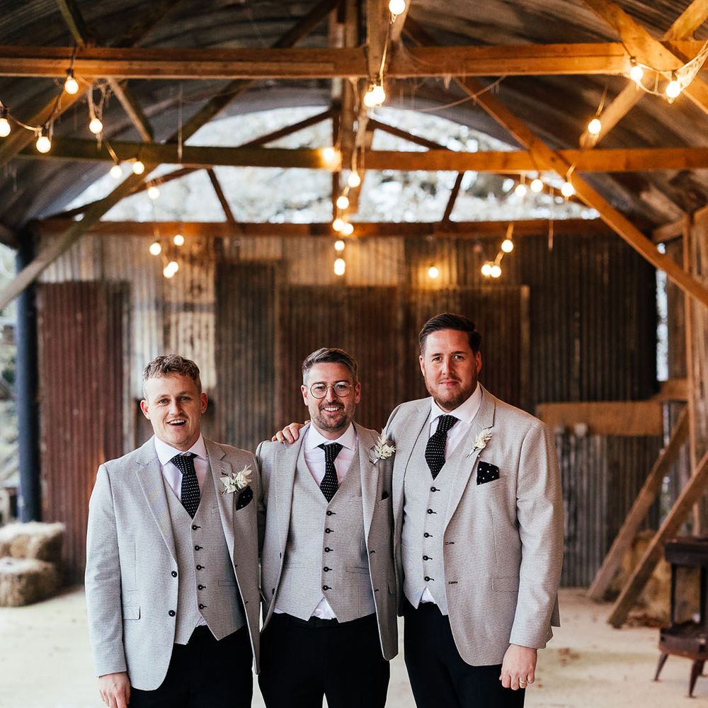 The groom and groomsmen standing together in light grey suit jacket and waistcoat with polka dot ties and handkerchief with white rose buttonhole