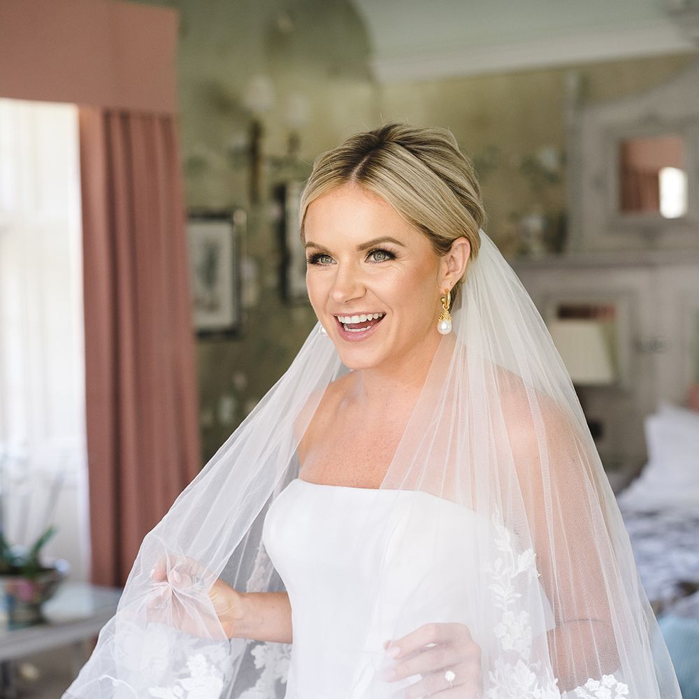 Bride with blonde hair in an updo wearing an embroidered edge wedding veil with pearl earrings 