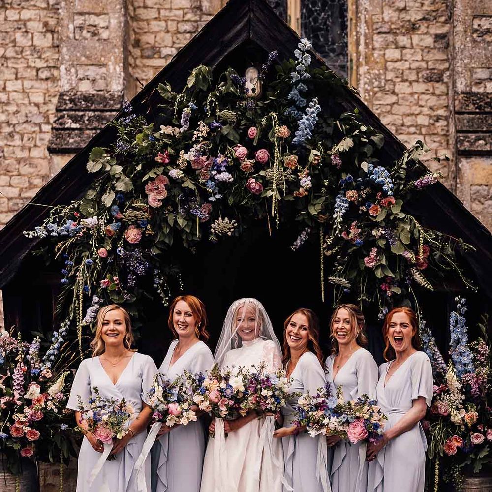 Bride in long sleeve classic wedding dress standing with bridal party in front wrap short sleeve blue bridesmaid dresses 