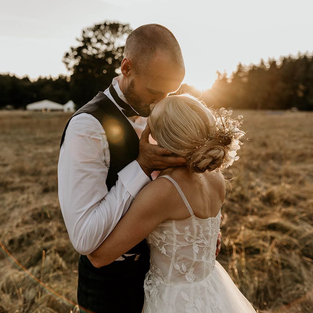 Golden hour wedding photo of the bride and groom at sunset with the bride wearing white flower hair accessory 