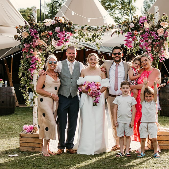 Pink wedding flower arch decorating the entrance to the tipi with the wedding guests