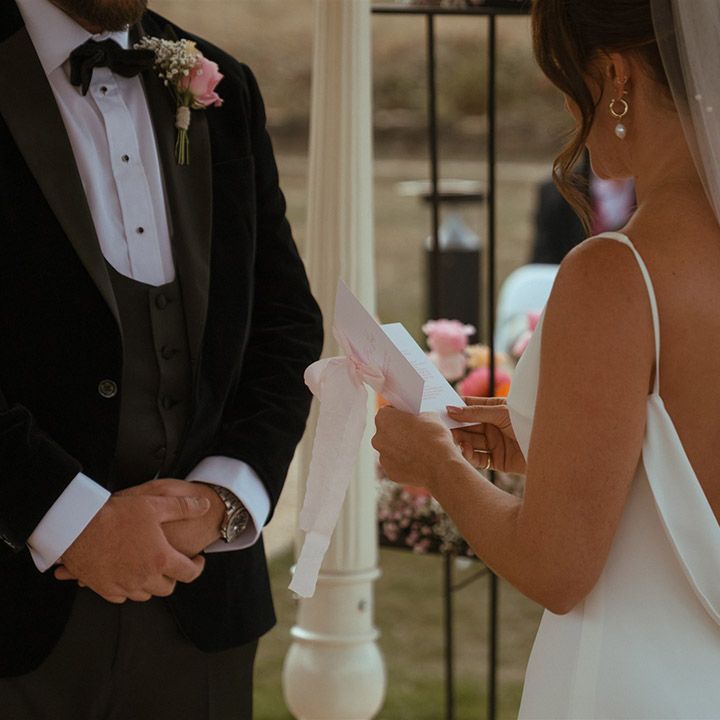 Bride in satin wedding dress with open back style and pearl wedding veil exchanging vows with the groom 