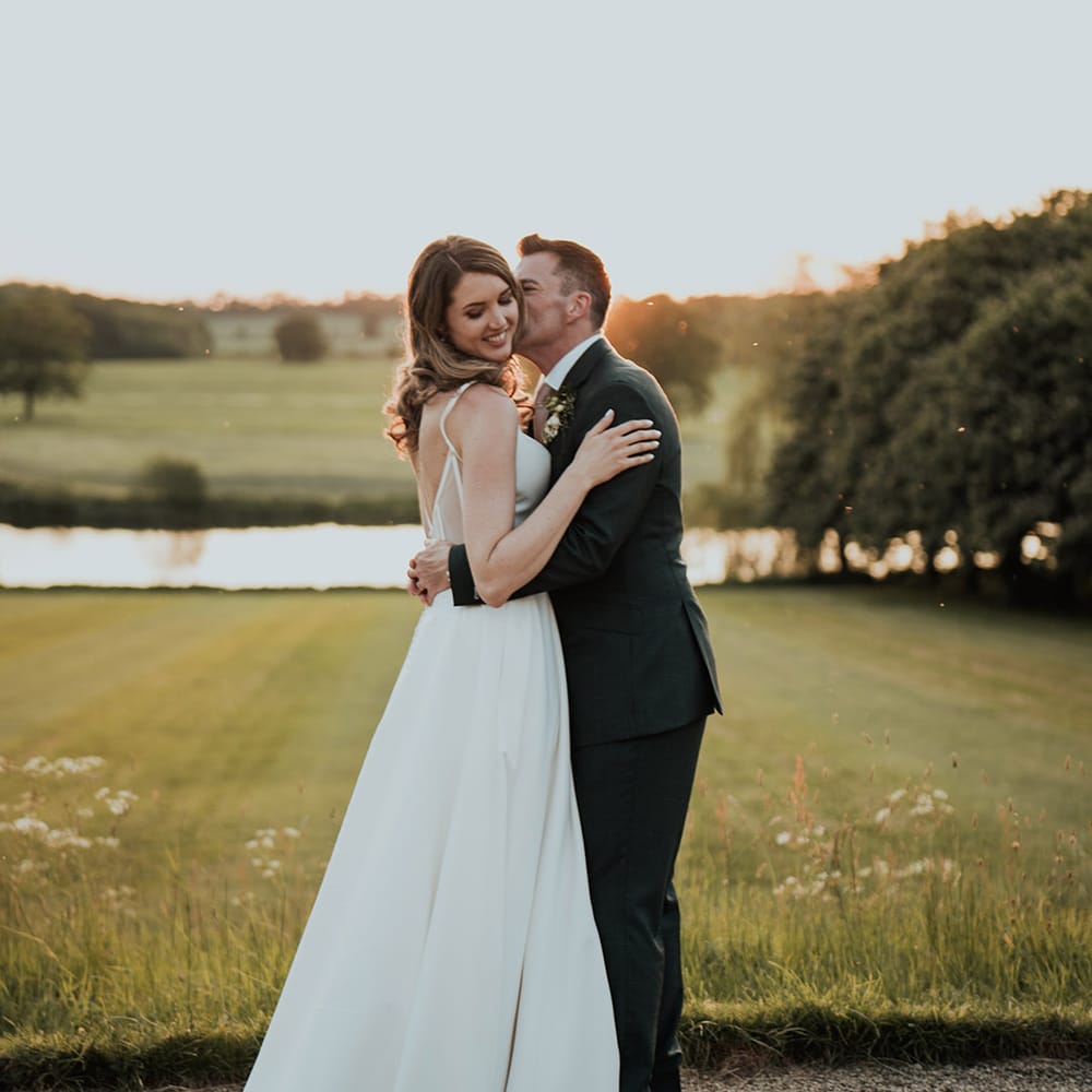 Kelmarsh Hall and Gardens wedding venue with the groom kissing the bride's cheek 