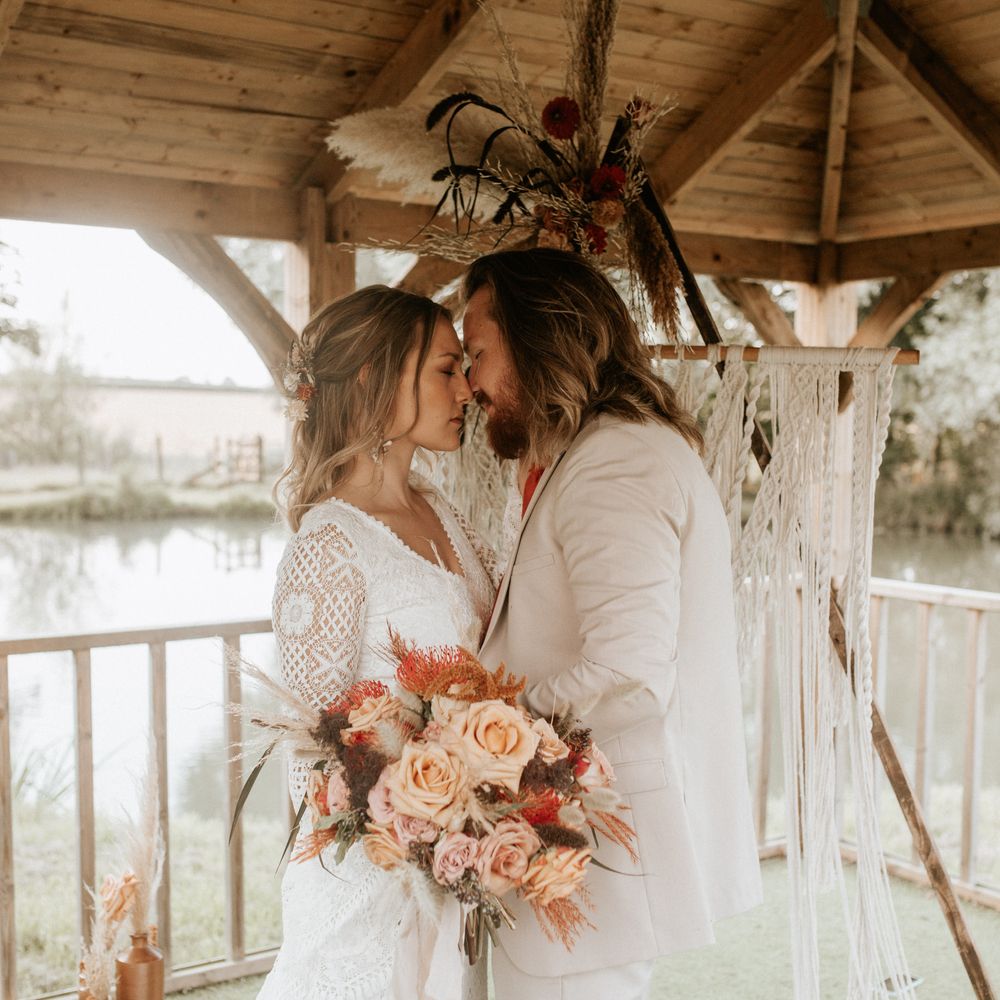 Bride & groom kiss with lake behind under wooden roof