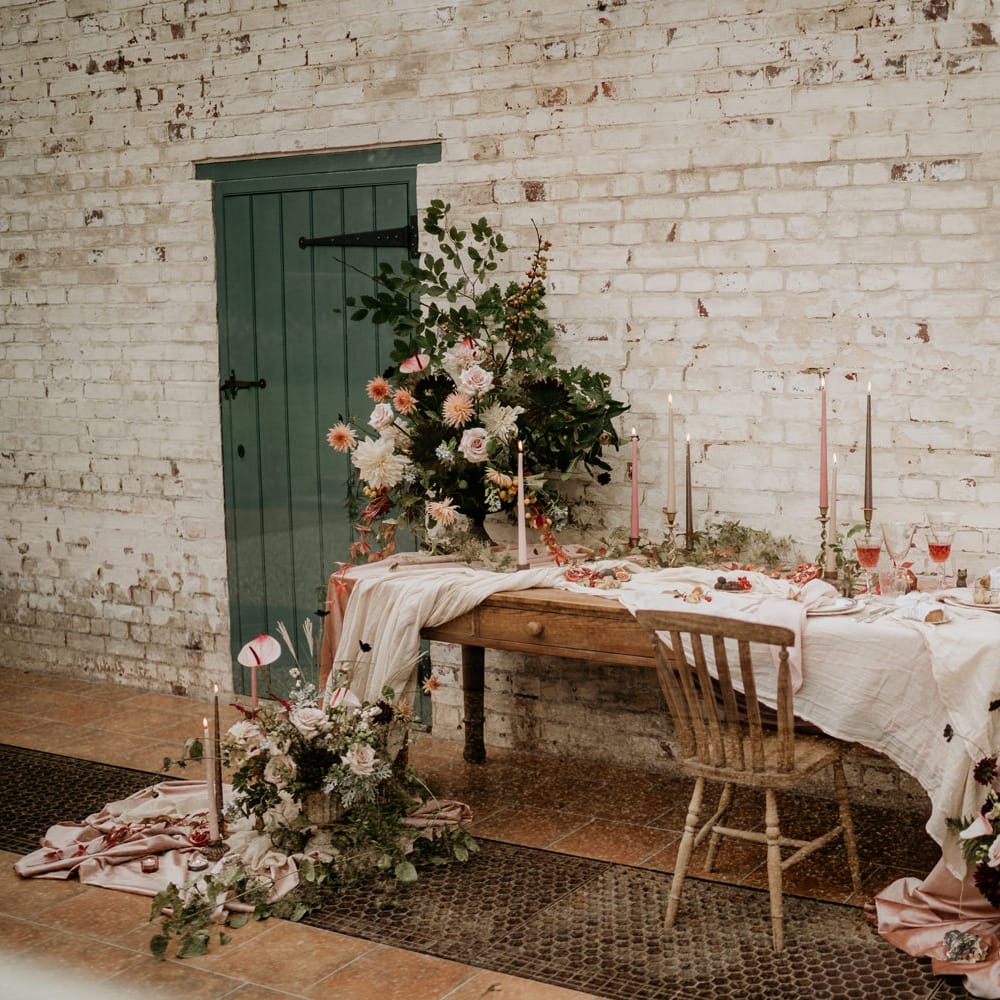 Intimate tablescape with blush pink table cloth, wooden chairs, taper candles and blush and green wedding flowers 