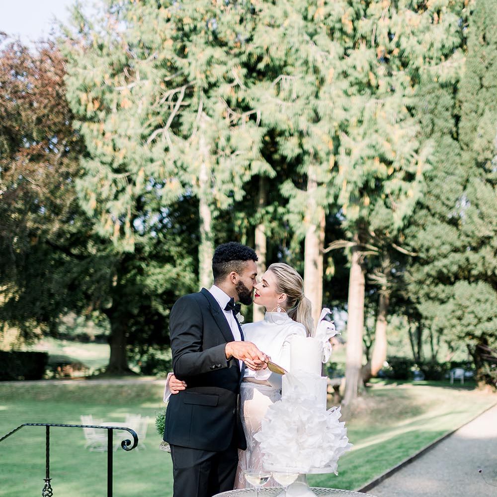 Bride and groom cutting the all white wedding cake outside 