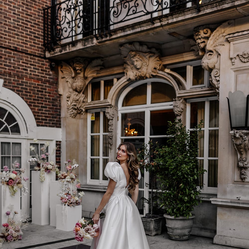 Bride in a taffeta Love In Lave bridal gown with puff sleeves standing in the courtyard at Dartmouth House wedding venue in Mayfair