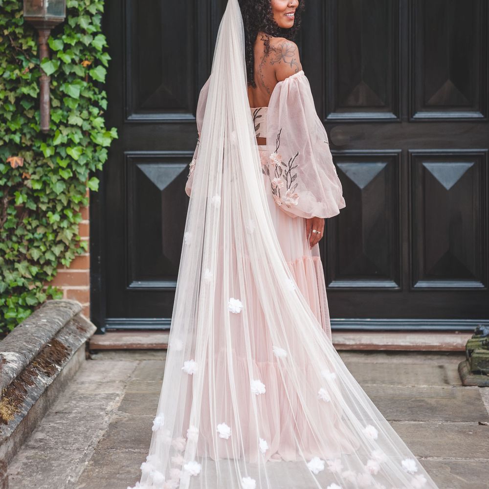 Black bride with long curly hair wearing a blush pink appliqué wedding veil 