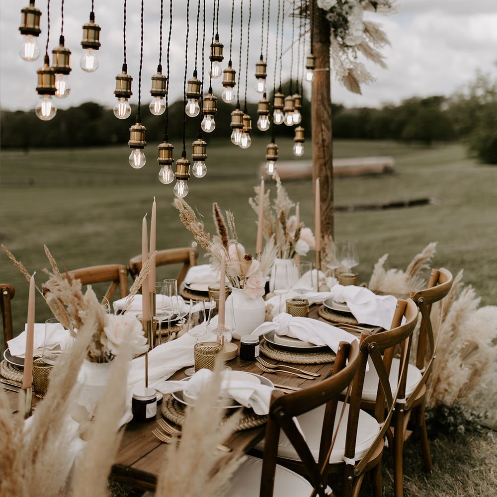 Hanging light installation over a boho tablescape with dried grasses, taper candles and coloured goblets 